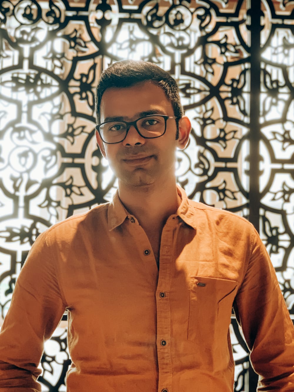 Sudarshan Thiagarajan in an ochre shirt, backlit by a carved screen